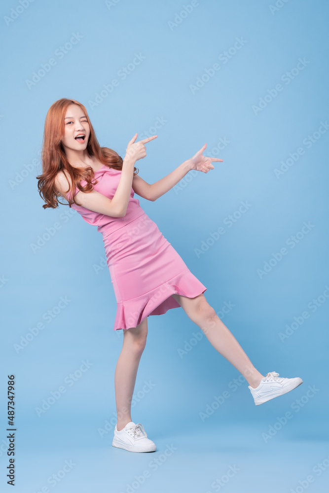 Young Asian woman wearing pink dress and posing on blue background