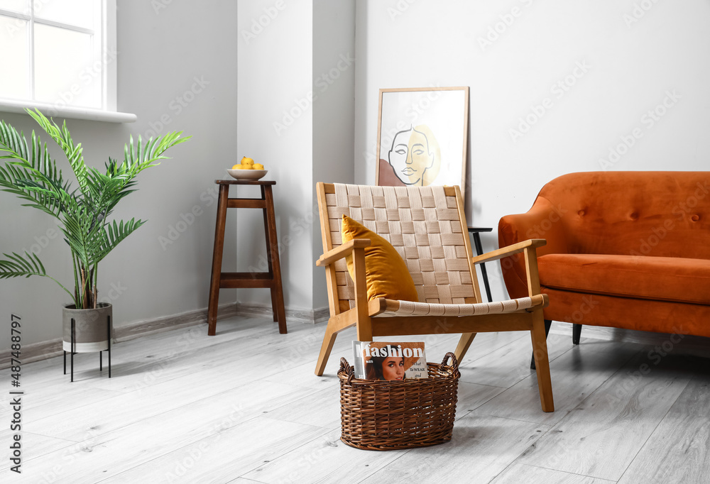 舒适的扶手椅和篮子，带杂志，位于明亮的客厅内部
