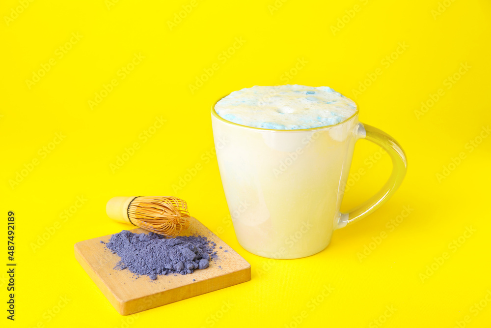 一杯蓝色抹茶拿铁，黄色背景的粉末和追逐