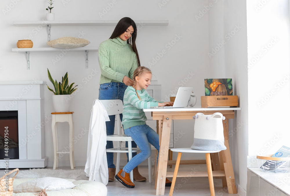 快乐的母亲和她穿着保暖毛衣的小女儿在家里用笔记本电脑