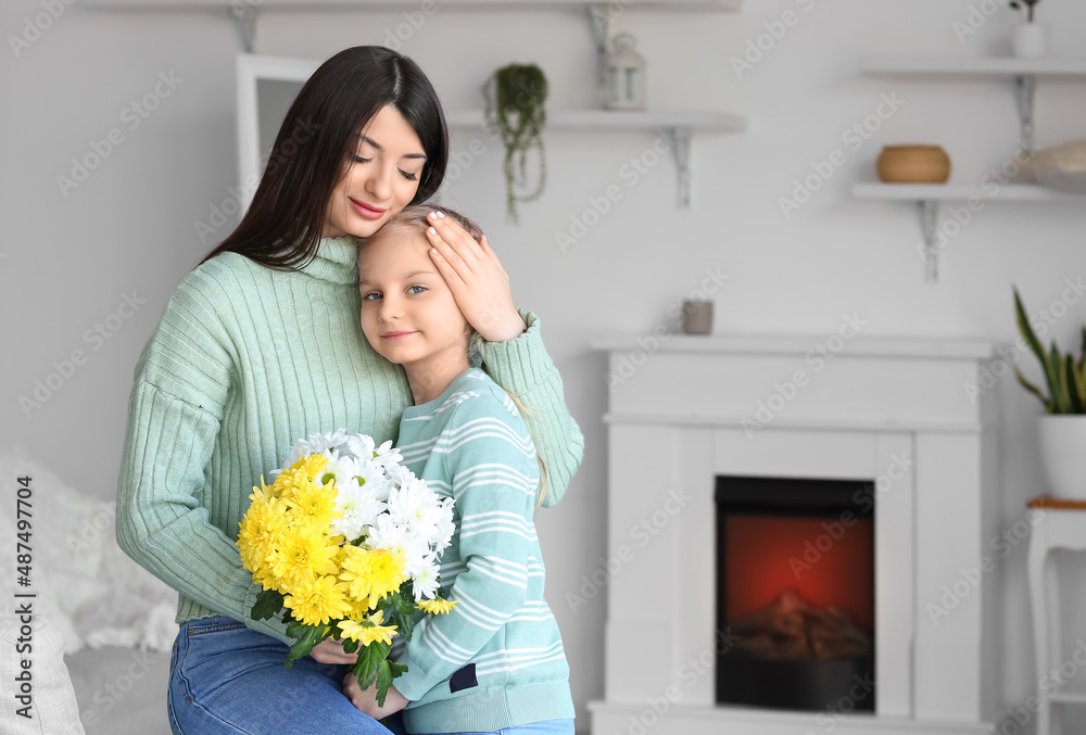 年轻的母亲和她的小女儿穿着毛衣，家里有花