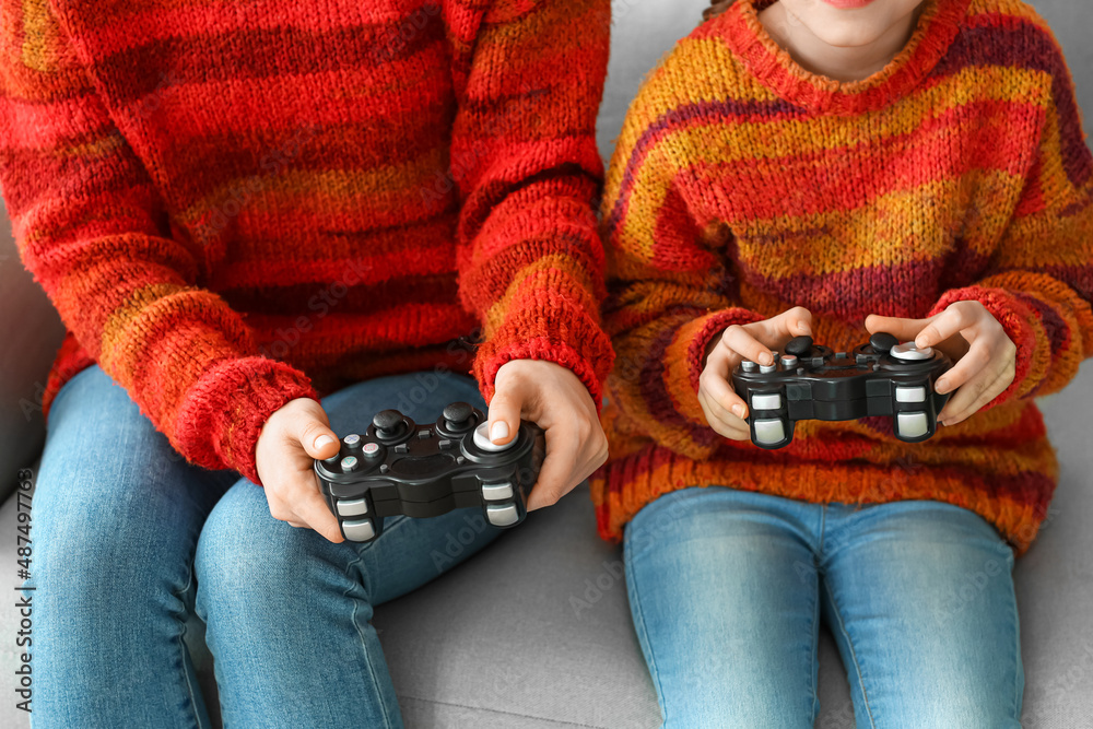 小女孩和她妈妈穿着暖和的毛衣在家玩电子游戏，特写镜头