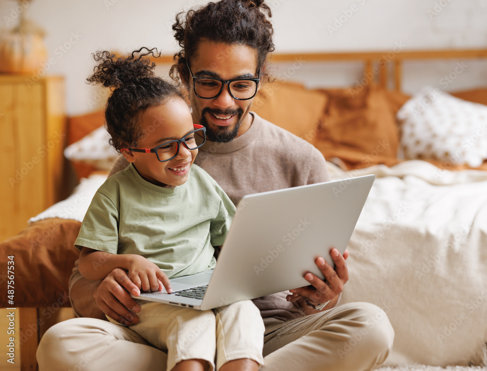 快乐的非裔美国人家庭小儿子和爸爸一起在家里用笔记本电脑看有趣的视频
