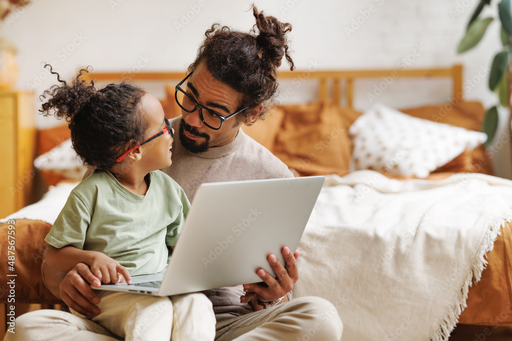快乐的美国黑人家庭小儿子和爸爸在家里一起在笔记本电脑上看有趣的视频