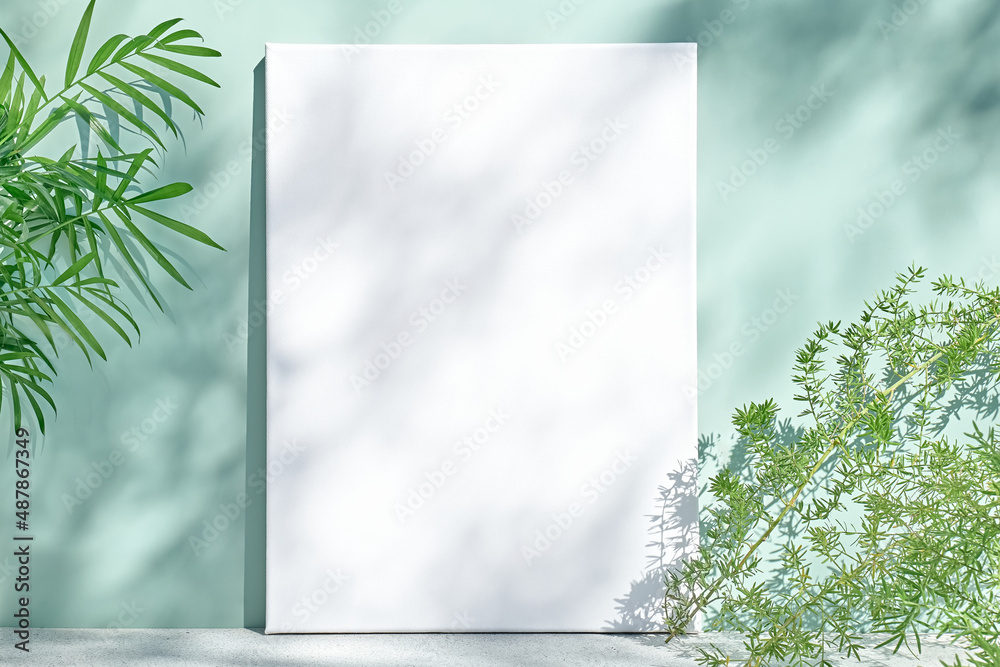 薄荷色表面上的空白白色绘画画布，带有棕榈叶、家庭植物和柔软的花朵沙