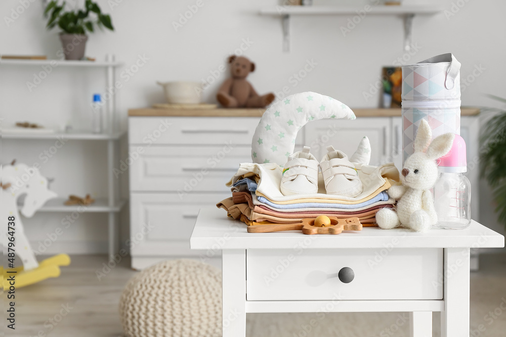 儿童房白色桌子上的一堆婴儿衣服、鞋子和玩具