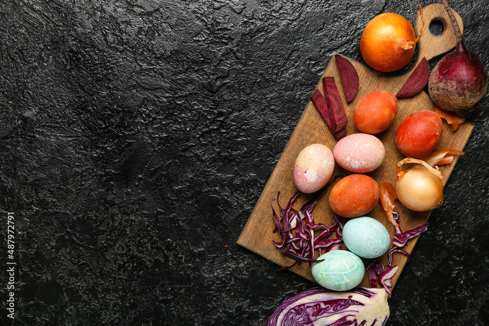 Wooden board with beautiful Easter eggs and natural dyes on dark background