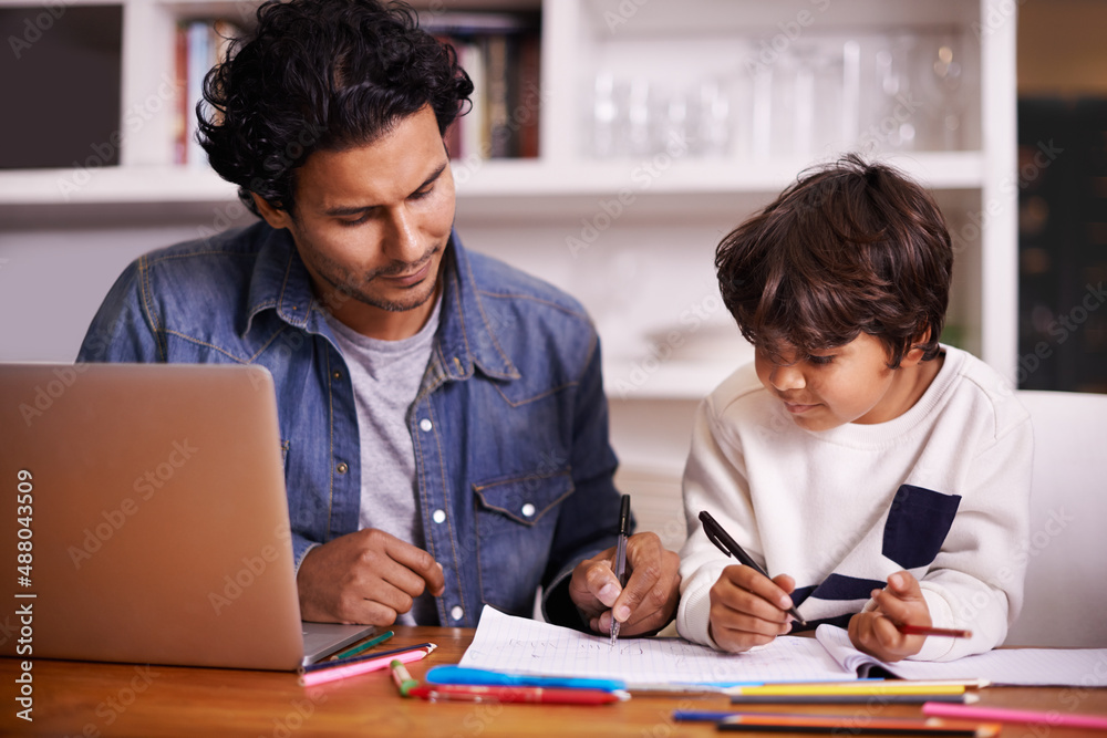 细心的指导会带来更大的回报。一个父亲帮助儿子做家庭作业的镜头。