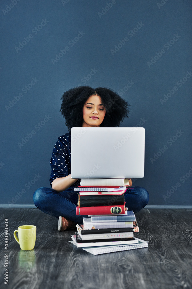 总是寻求知识。一名年轻女子使用笔记本电脑的工作室镜头，笔记本电脑前面堆着书。