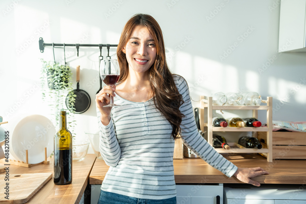 亚洲美女，在家厨房里用玻璃杯喝酒。
