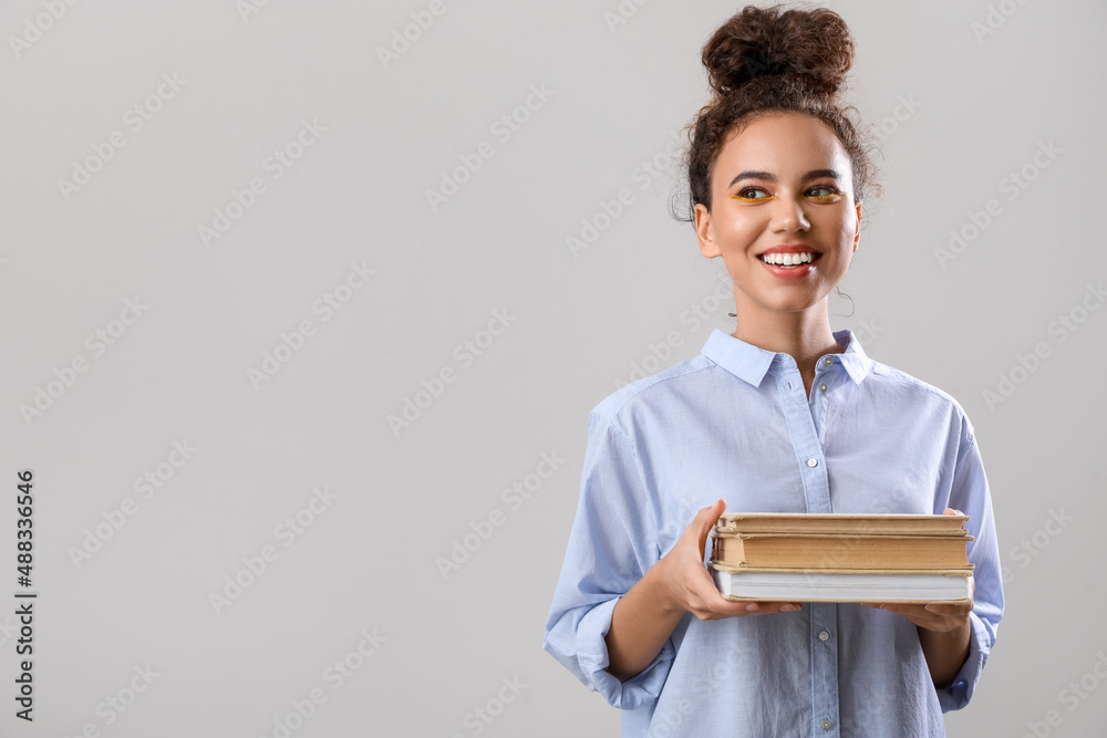 美丽的年轻非裔美国女性，灰色背景下有书