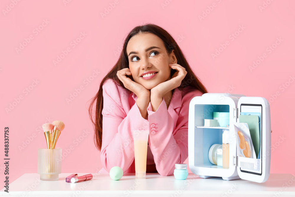 漂亮的年轻女人，拿着小冰箱和化妆品坐在桌子旁的彩色靠背上