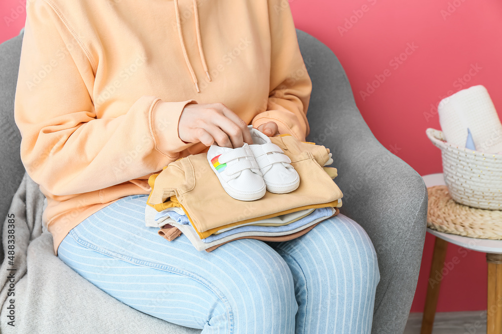 坐在扶手椅上的女人，手里拿着一堆婴儿衣服和鞋子