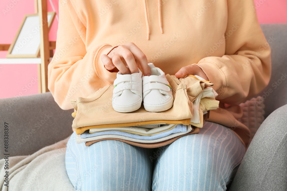 坐在扶手椅上的女人，手里拿着一堆婴儿衣服和鞋子，特写