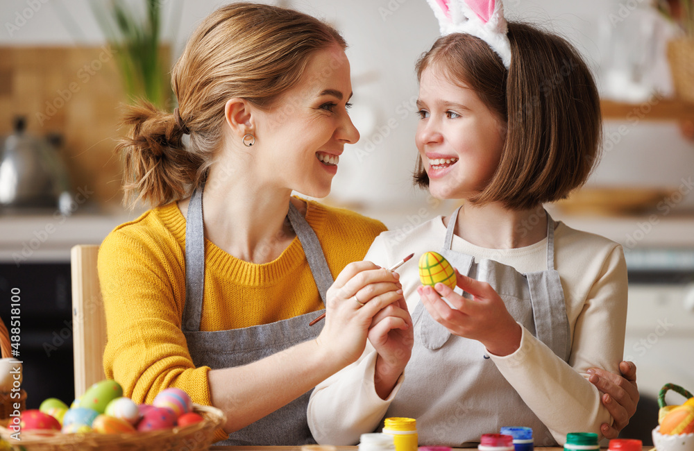 慈爱的年轻母亲坐在厨房里教快乐的小女儿装饰复活节彩蛋
