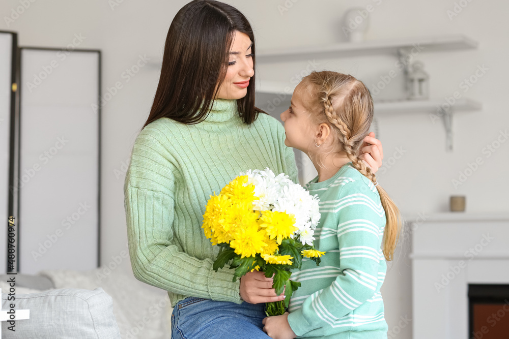 年轻的母亲和她的小女儿穿着毛衣，家里有花