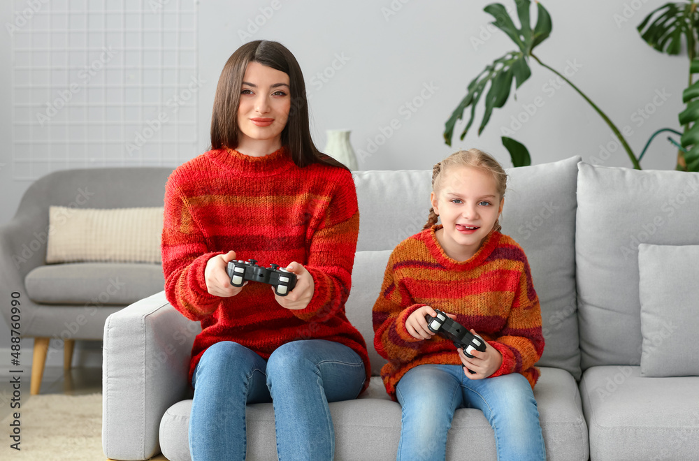Little girl and her mother in warm sweaters playing video game at home