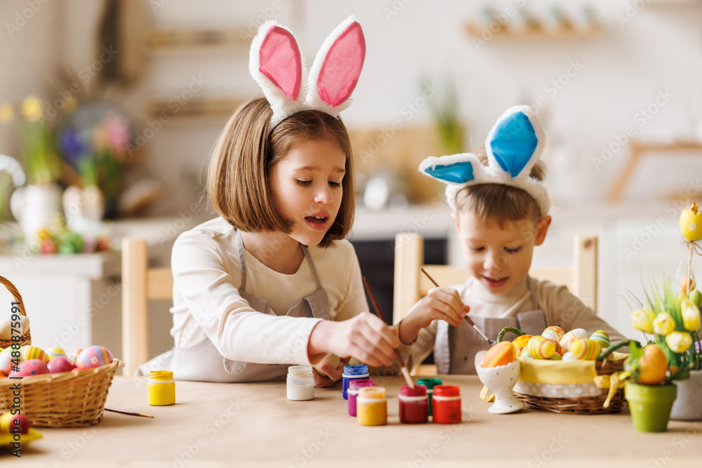 好奇的孩子们，戴着兔子耳朵的兄弟姐妹在厨房里一起画复活节彩蛋