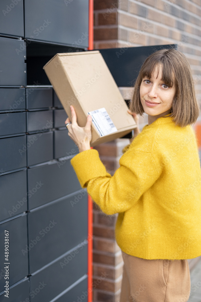 Young woman getting parcel from cell of automatic post terminal outdoors. Concept of contactless and