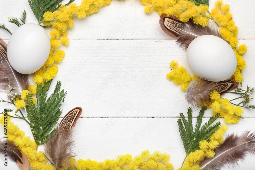 由含羞草花、叶子、羽毛和鸡蛋制成的复活节花环，白色木背景，特写
