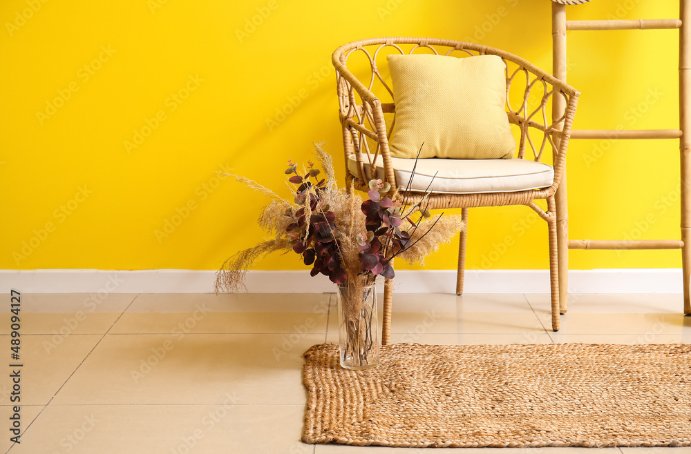 Wicker chair, vase with dry flowers and stylish carpet in room interior