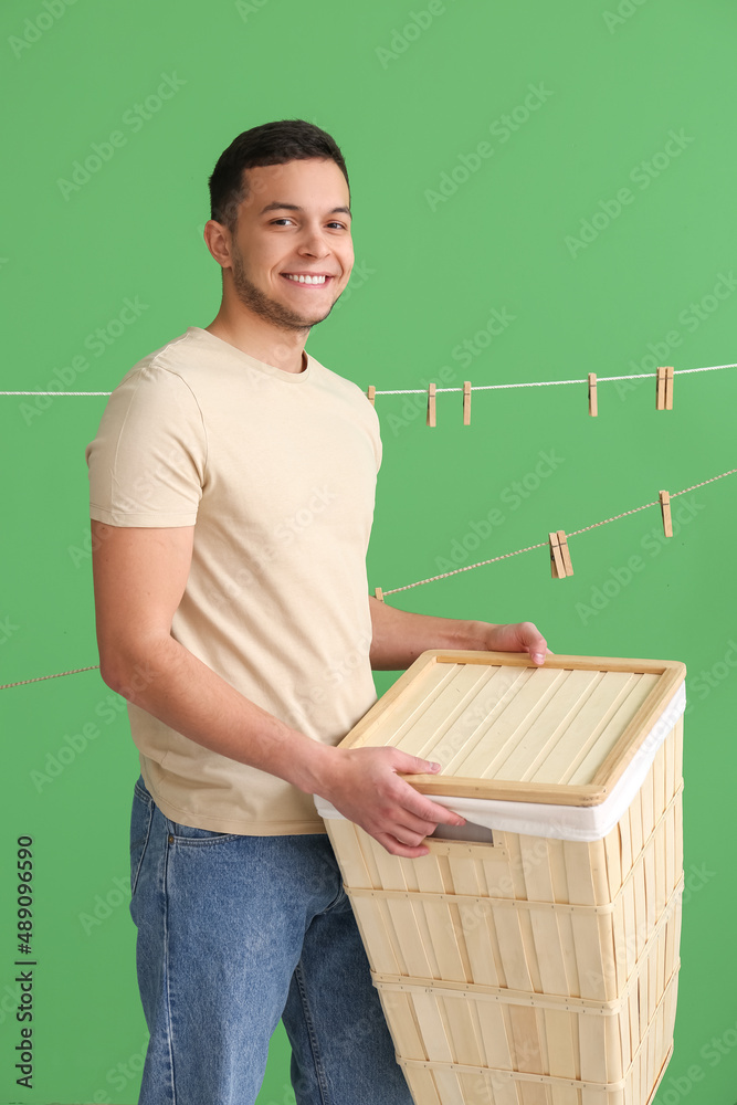 Young man with laundry basket and hanging clothespins on green background