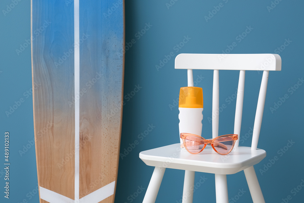 彩色墙壁附近的椅子和冲浪板上的一瓶防晒霜、太阳镜