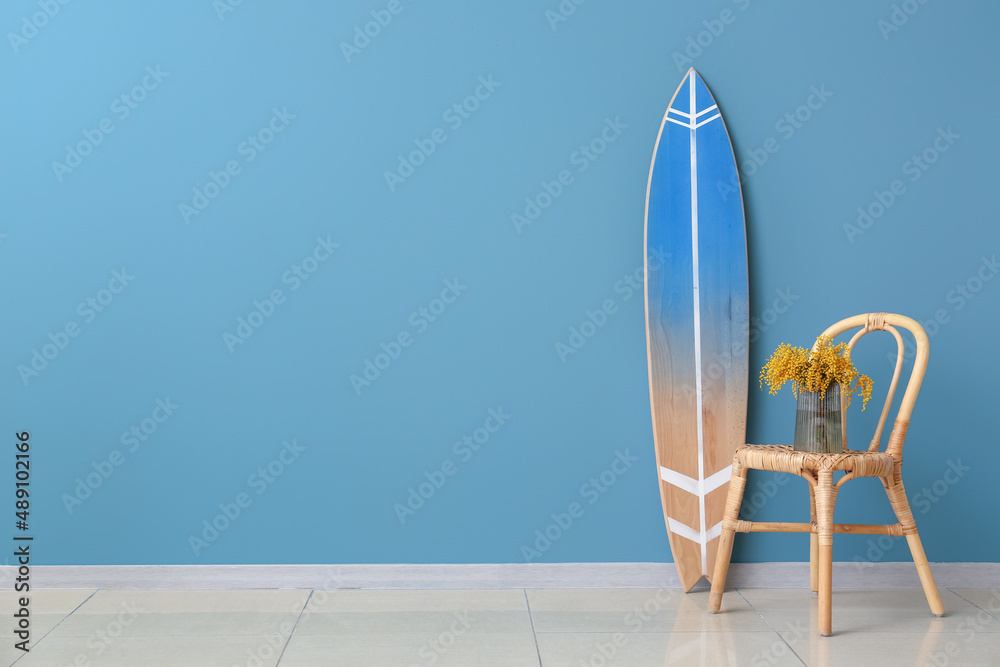房间彩色墙壁附近的椅子和冲浪板上有含羞草花的花瓶