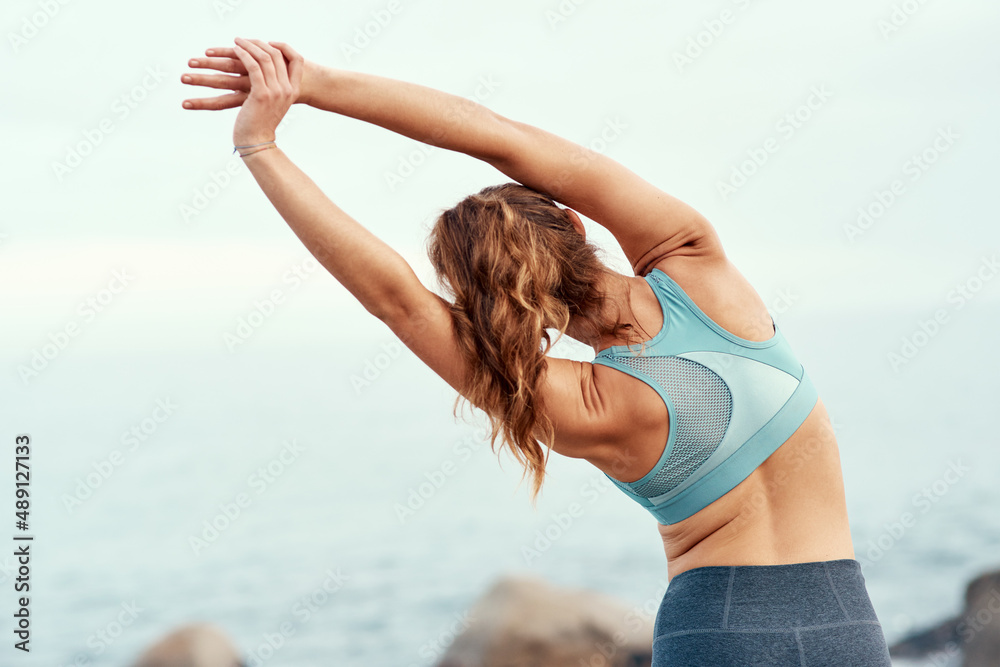 Feel the flow of the day. Rearview shot of a sporty young woman stretching her arms while exercising