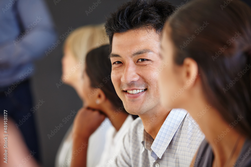 Getting a stand out idea. Shot of an Asian man sitting at a table with his coworkers out of focus.