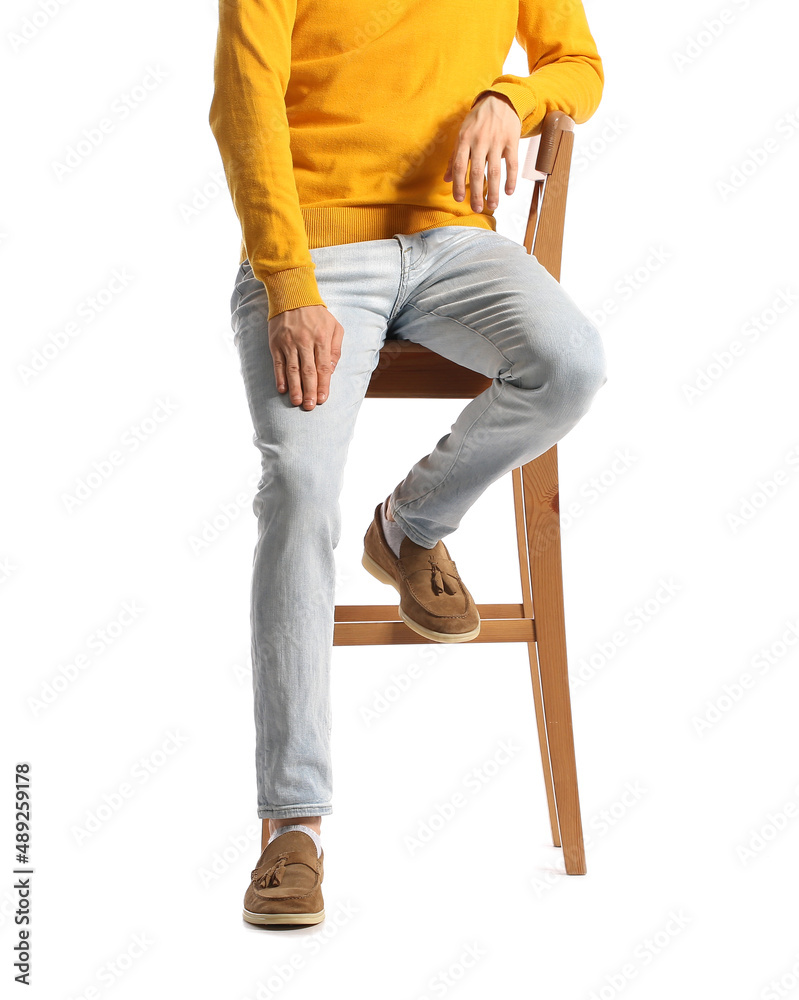 穿着时尚牛仔裤的时尚年轻人坐在白底椅子上