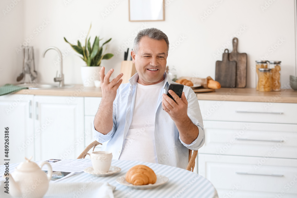 Senior man using mobile phone at table in kitchen