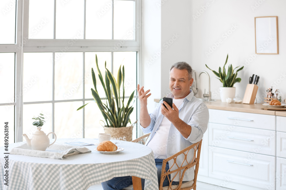 Senior man using mobile phone at table in kitchen