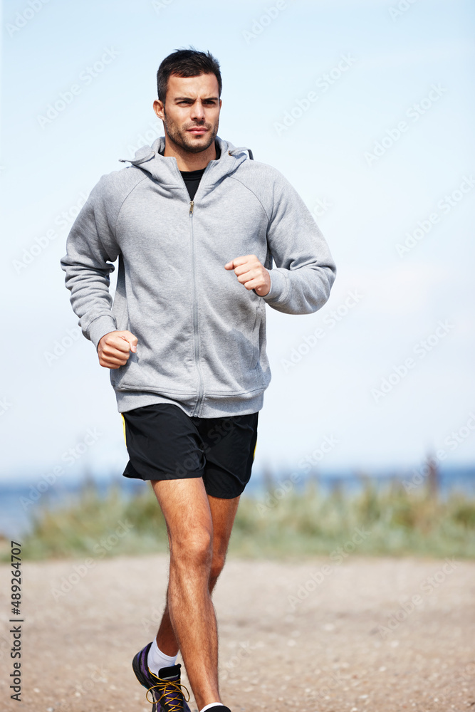 早上在海滩上慢跑。一个英俊的年轻人在海滩上跑步的镜头。