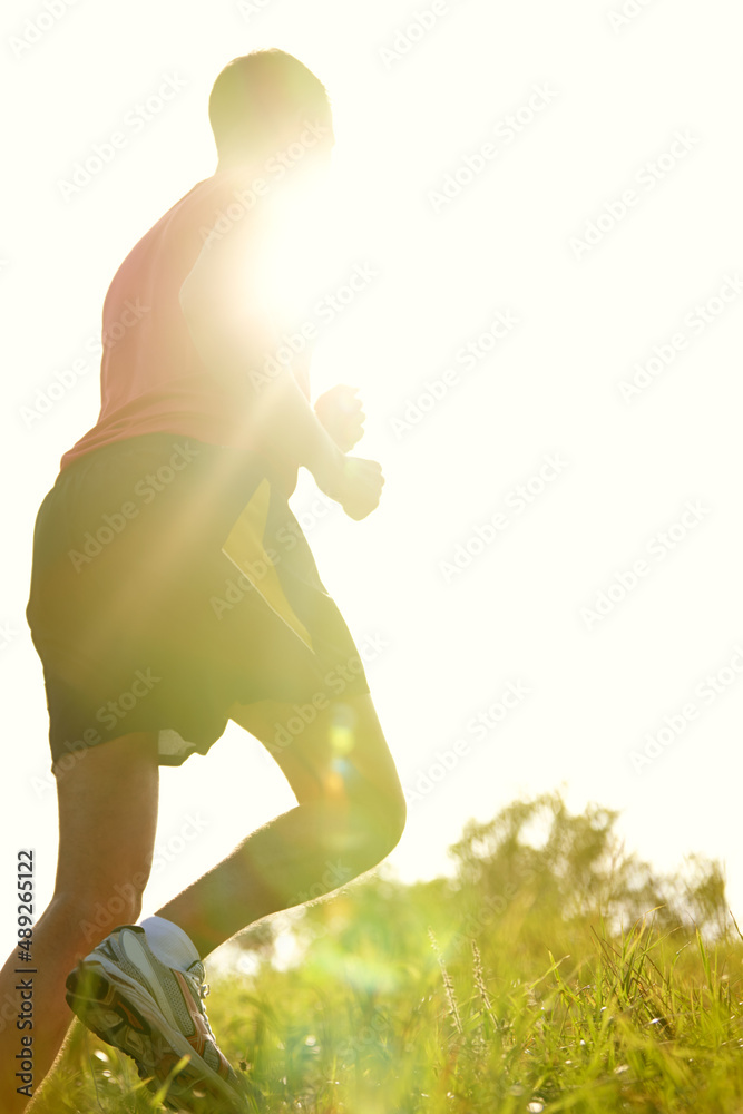 在阳光下跑步。一个年轻人在户外山路上跑步的后视镜头。