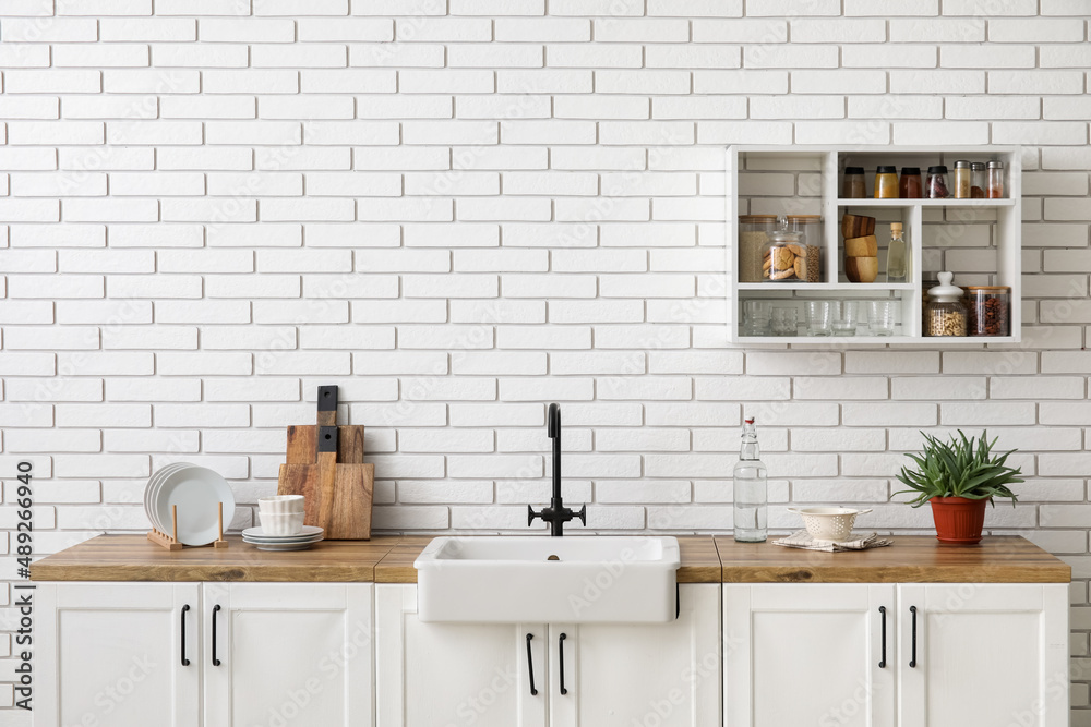 白色砖墙上挂着带水槽、厨房用具和搁架的柜台