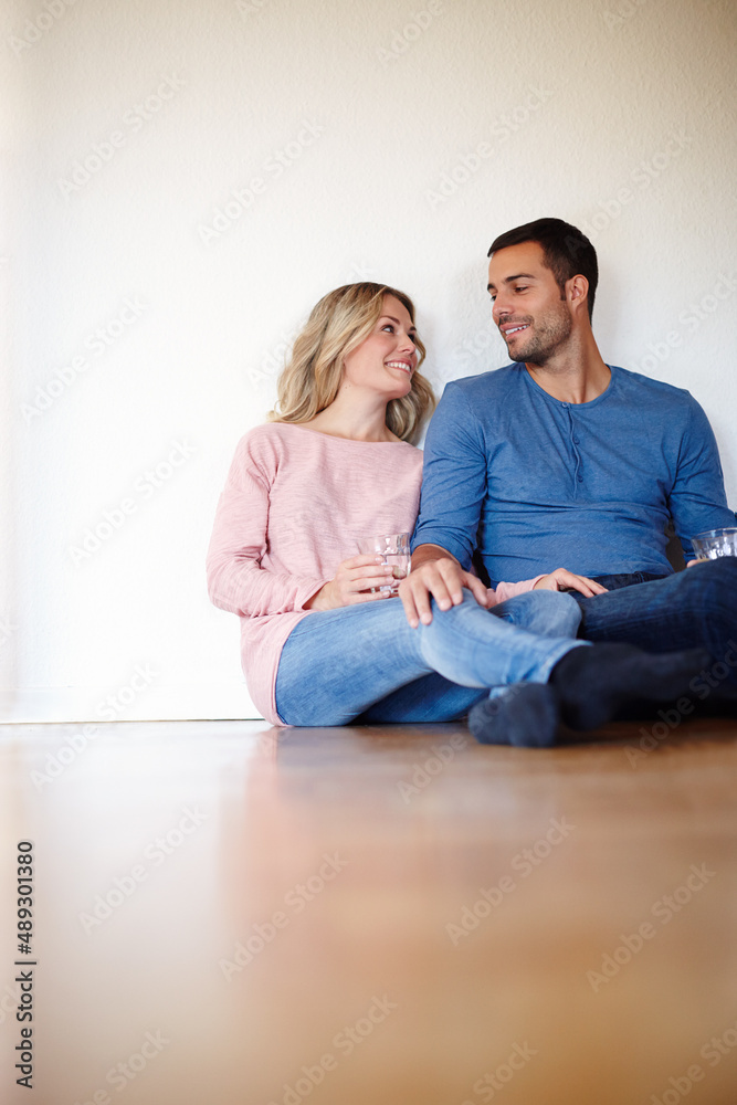 在他们的新家里很开心。一对幸福的年轻夫妇坐在客厅地板上的照片。