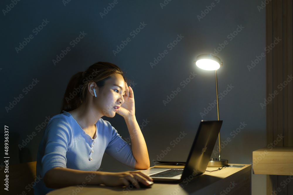 亚洲女性因笔记本电脑或笔记本电脑上的项目研究问题而工作到深夜，压力很大