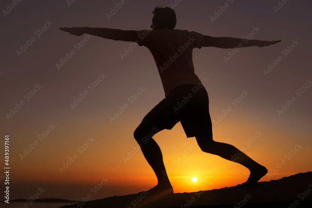 在昏暗的光线下伸展身体。一个男人在日落的背景下锻炼身体的剪影