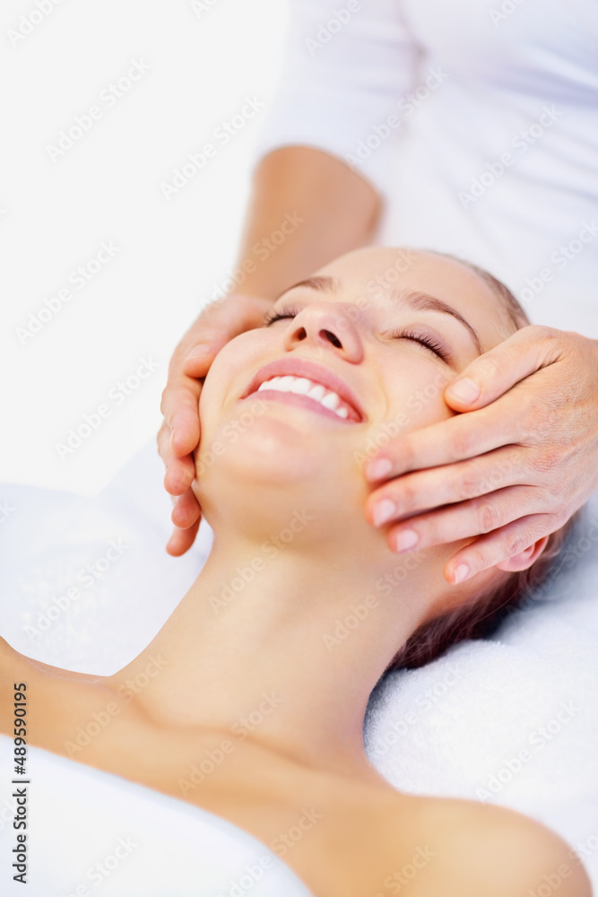 快乐的女性接受按摩师的面部按摩。微笑的年轻女性享受按摩