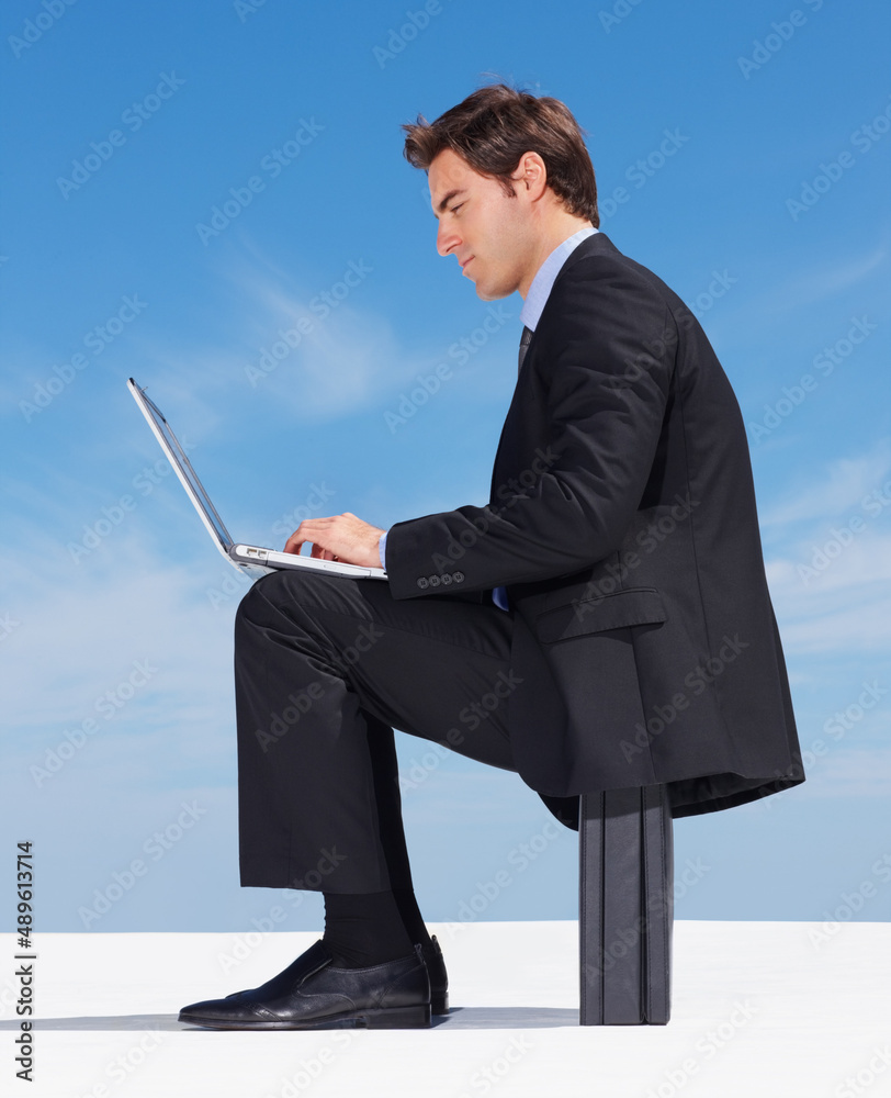年轻的高管在晴朗的天空下用笔记本电脑工作。一位成功的年轻商人的侧视图
