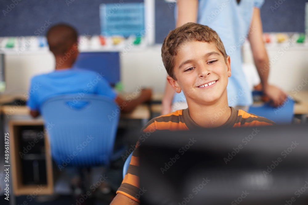 在电脑屏幕上检查他的作品。电脑课上一个可爱的年轻男生。