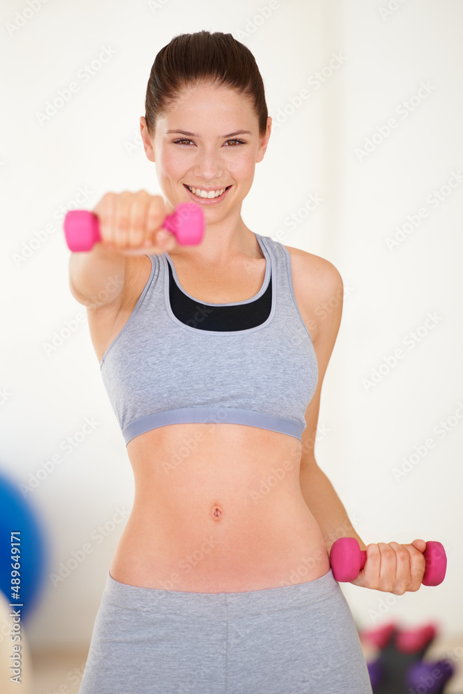 塑形。一位年轻漂亮女子在健身房用哑铃训练的肖像。