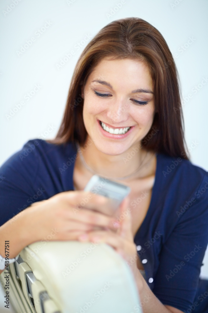 Enjoying a humorous text from a friend. A beautiful young woman sending a text message from her mobi