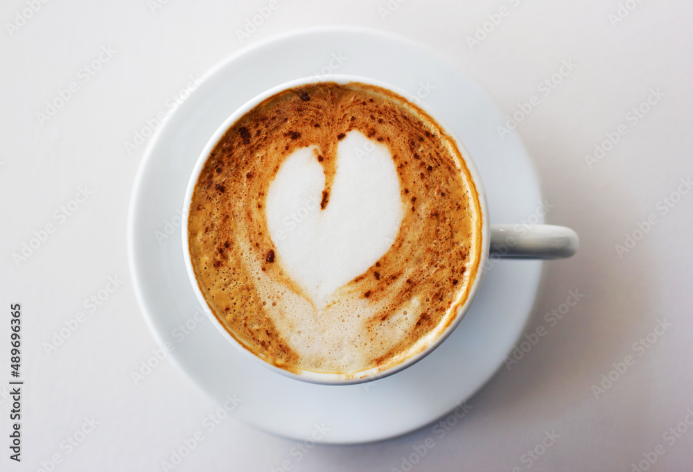 The best start to any morning. A freshly-made cappuccino on a white table with a heart shape in the 
