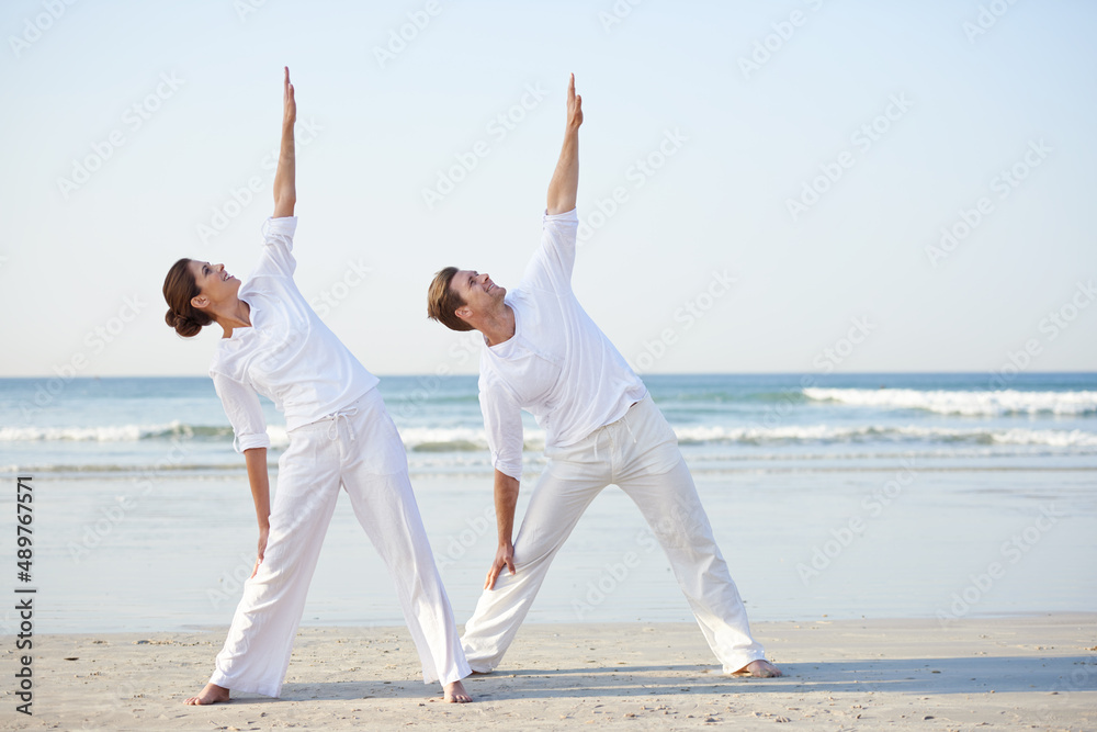 海边瑜伽。一对年轻夫妇在海滩上练习瑜伽。