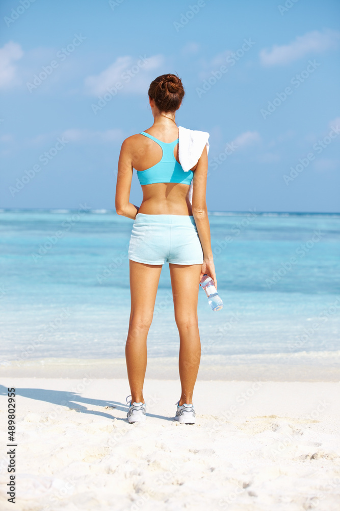 锻炼后放松。健康的年轻女子面朝大海站着的后视图。