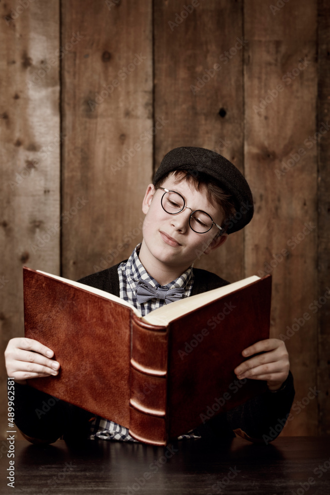 Learning lots of new things. Young boy in retro clothing wearing spectacles reading a massive book t