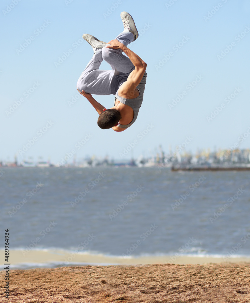 上下颠倒。一个运动型年轻人在海滩上翻筋斗。