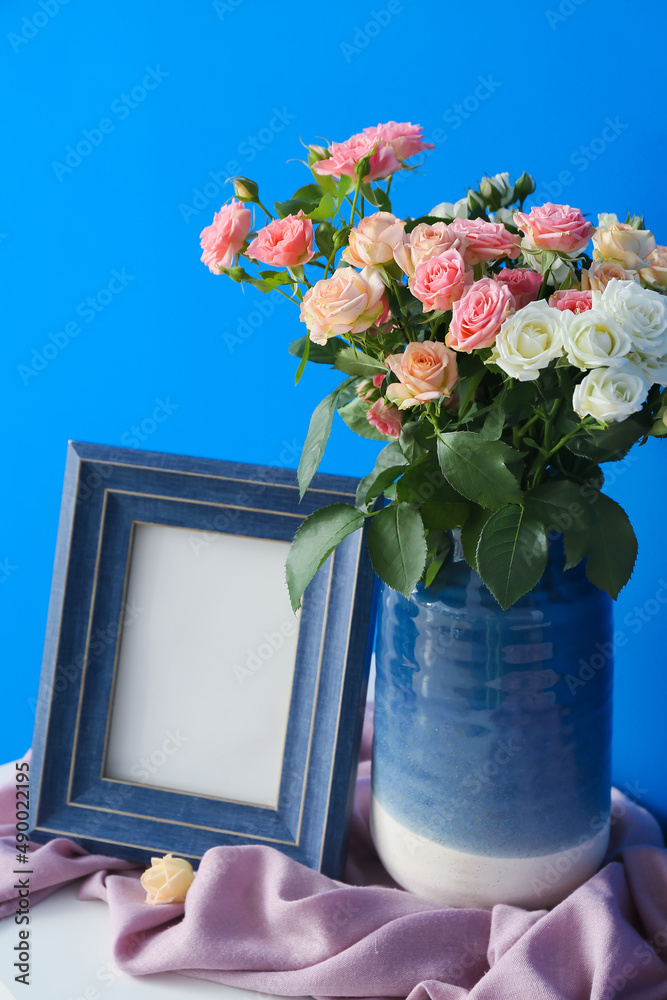 蓝色墙壁附近的架子上放着一个花瓶，上面有美丽的玫瑰、框架和粉色围巾